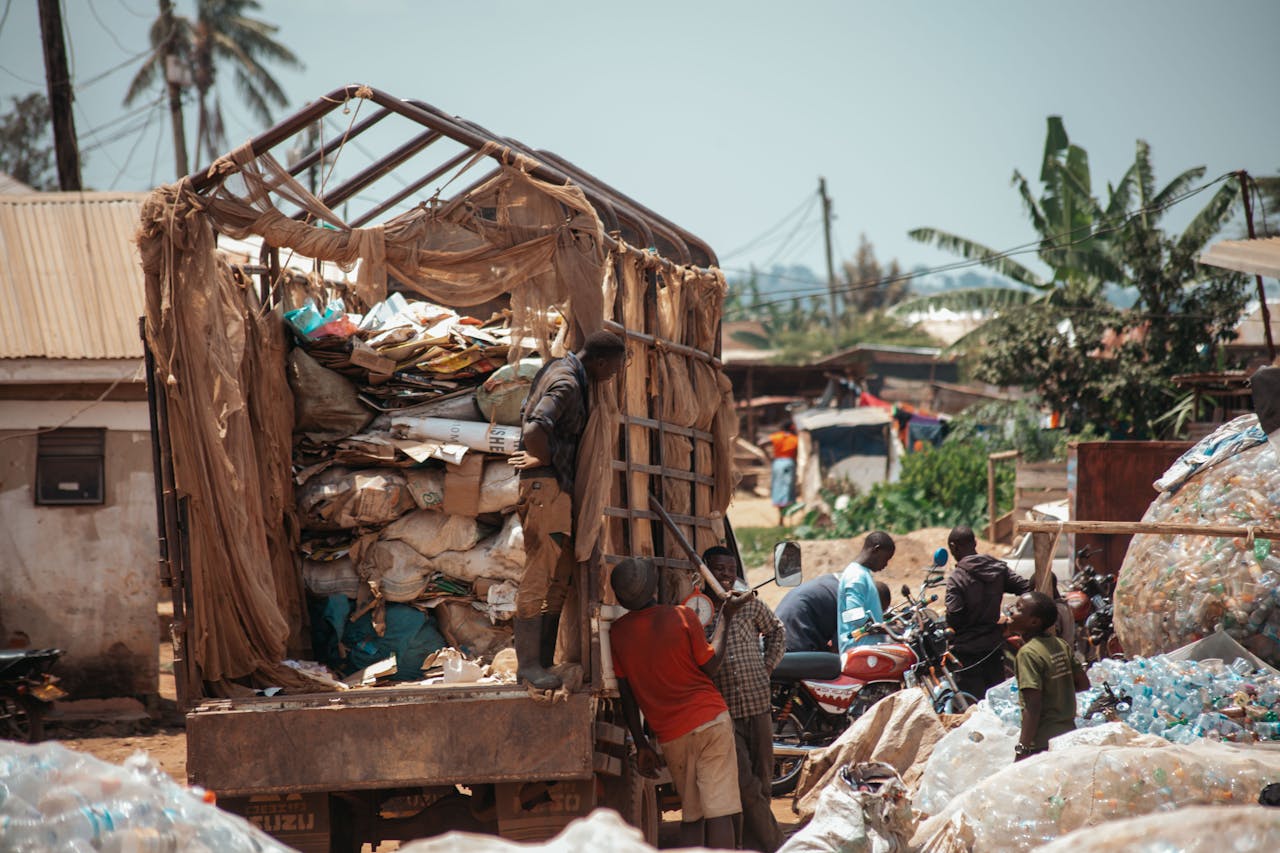 Men sorting recyclables at a landfill with piled plastic bottles and waste paper.